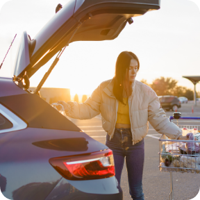 A woman loads groceries into the open hatch of her SUV. 